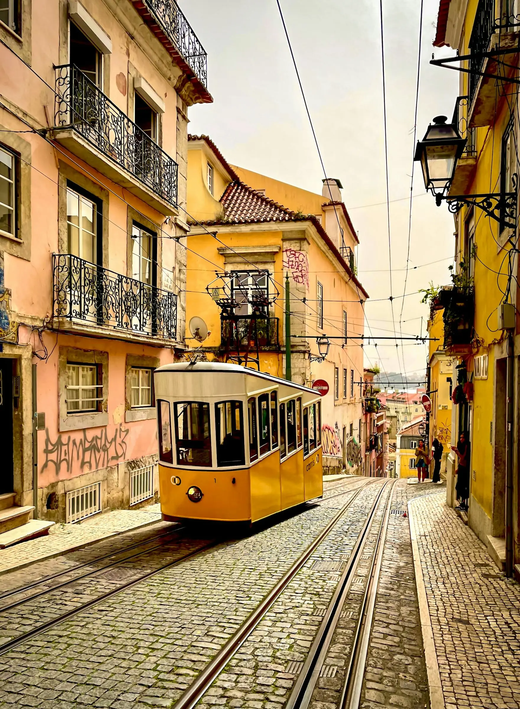Tramway jaune remontant une rue en pente de Lisbonne en fin de journée