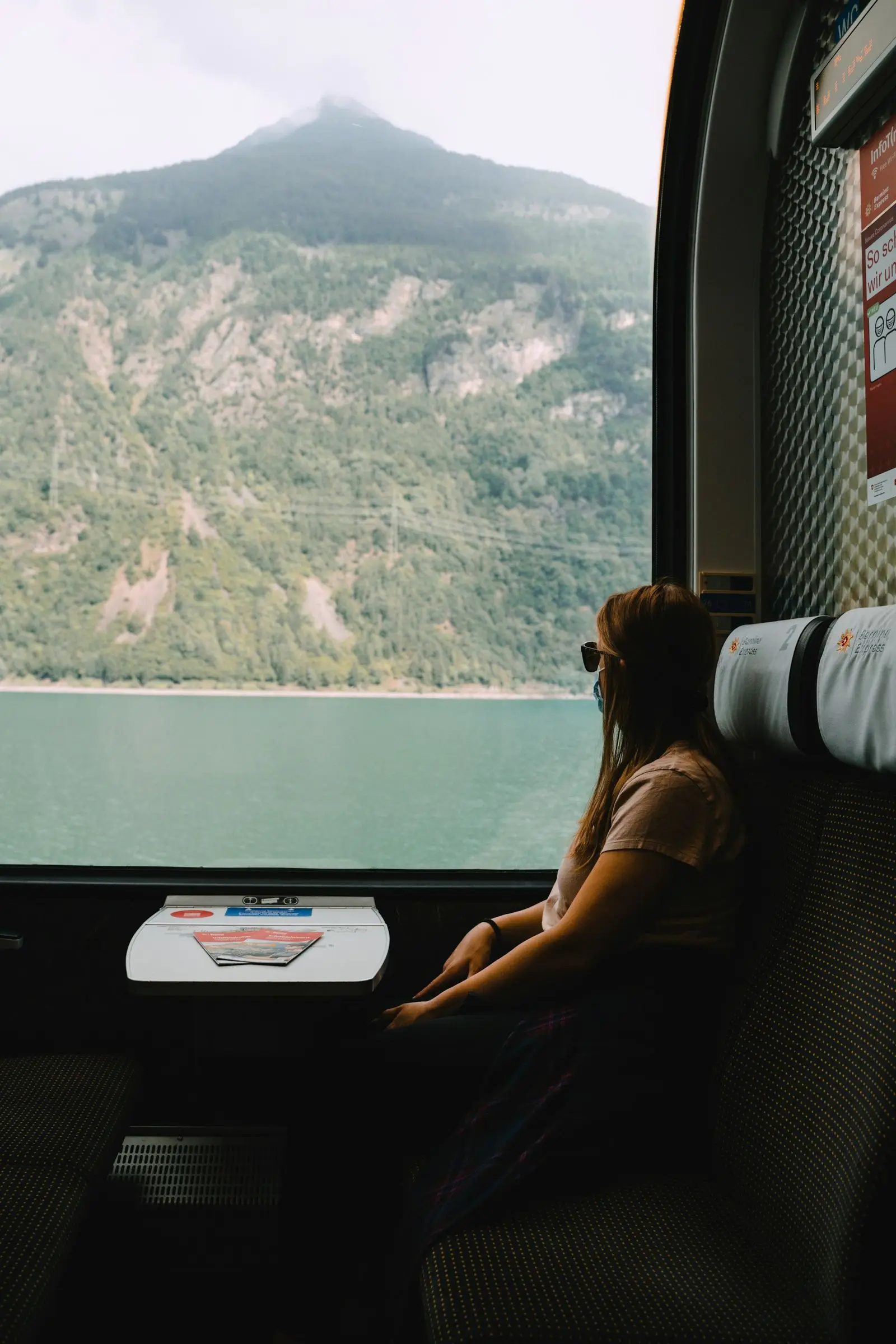 Voyageuse assise près de la fenêtre d'un train longeant un lac de montagne